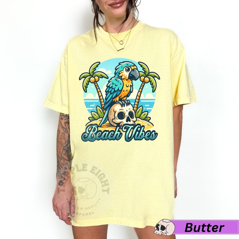 May include: A yellow t-shirt with a cartoon illustration of a blue and green parrot sitting on a skull with palm trees and the text "Beach Vibes".