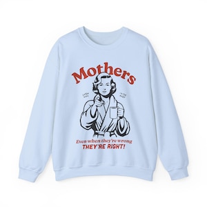 Op de afbeelding: Lichtblauwe trui met een zwart-witte illustratie van een vrouw in een badjas die een mok vasthoudt. De tekst "Mothers" staat in rode letters boven de illustratie. De tekst "Listen Kids I'm the Boss" staat in kleinere rode letters onder de illustratie. De tekst "Even when they're wrong THEY'RE RIGHT!" staat in rode letters onder de illustratie.