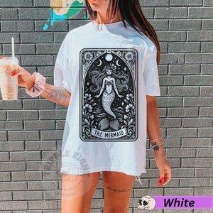 May include: White oversized t-shirt featuring a black and white graphic of a mermaid in a tarot card style design. The text "The Mermaid" is printed below the image.