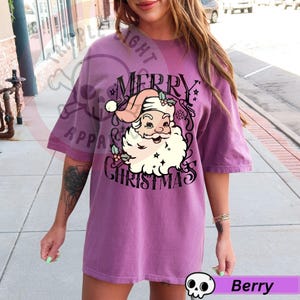 May include: Berry-colored t-shirt with a graphic of Santa Claus and the words "Merry Christmas." The Santa illustration features a pink hat, white beard, and holly accents. The shirt has short sleeves and a relaxed fit.