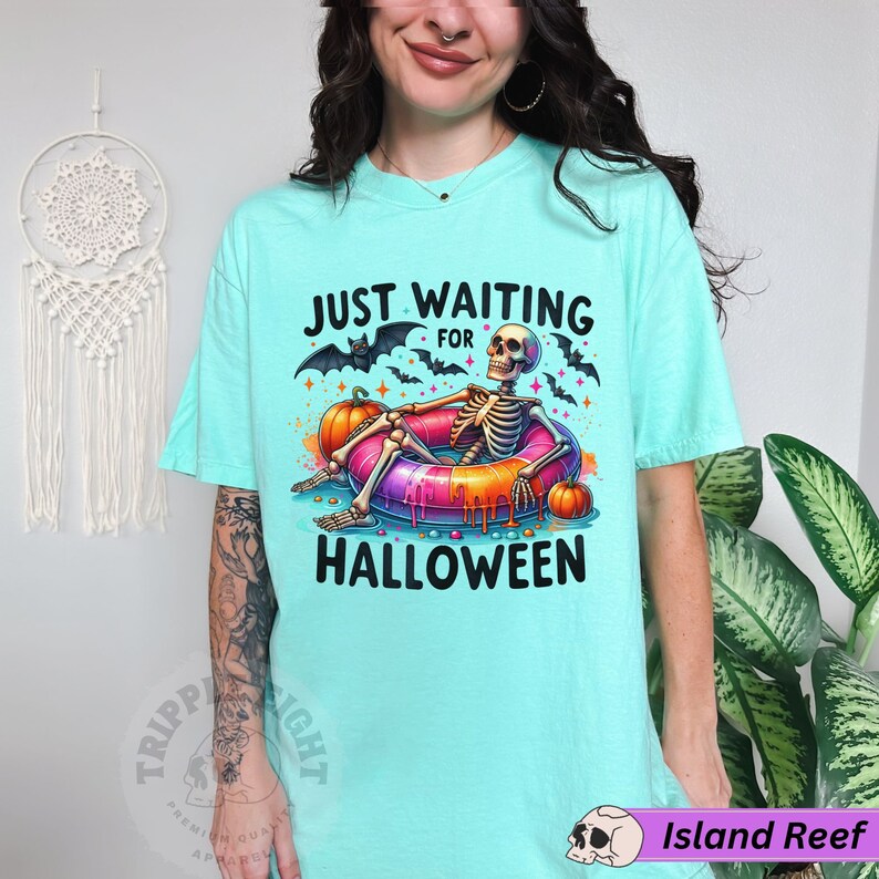 May include: A turquoise t-shirt with the text "Just Waiting For Halloween" and a skeleton in a pink and orange inflatable ring with pumpkins and bats.