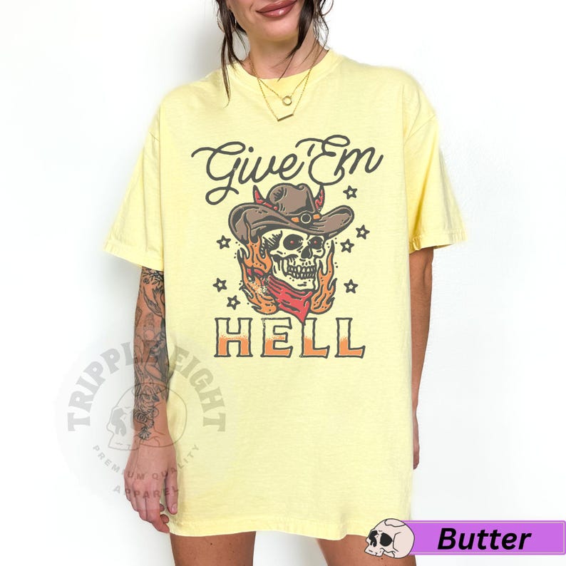 May include: Yellow t-shirt featuring a skull wearing a cowboy hat and flames. The text "Give 'Em Hell" is printed on the shirt.