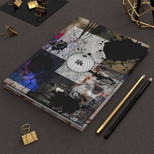 May include: A black and white notebook with a colorful abstract design and the word "life" on a globe. The notebook is on a gray surface with gold paper clips and pencils.