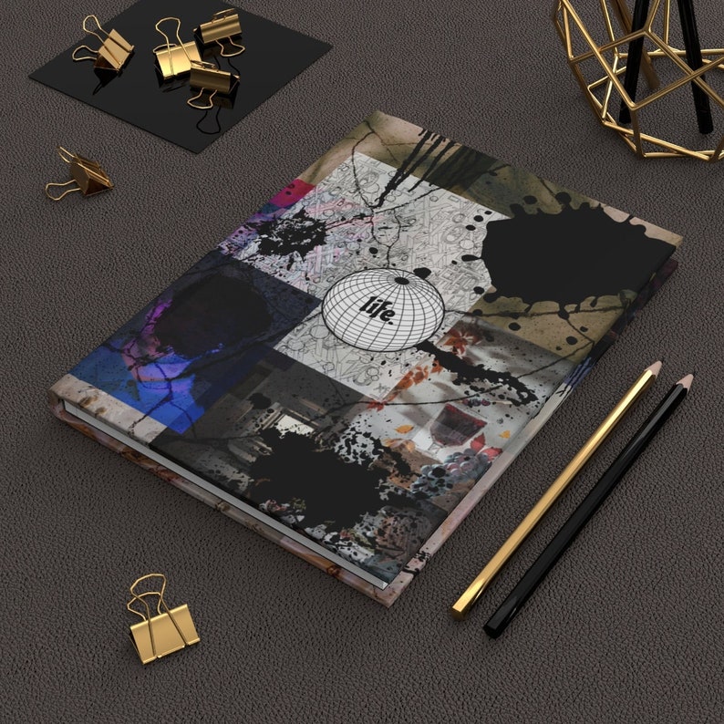 May include: A black and white notebook with a colorful abstract design and the word "life" on a globe. The notebook is on a gray surface with gold paper clips and pencils.