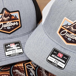 May include: Two gray and black trucker hats with a mountain and the word "Outdoor" on a patch. The hats are both labeled "Richardson" and have a size tag.