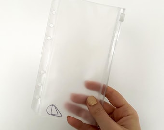 May include: Clear plastic zippered pouch with six holes down the left side for a binder. The pouch is held in a hand.