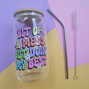 May include: A clear glass jar with a wooden lid and a colorful graphic that reads "Bit of a mess but doin' my best". The jar is accompanied by a metal drinking straw and a cleaning brush.