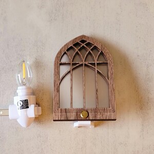 May include: A decorative night light featuring a wooden arched window design with a warm, inviting glow. The night light has a white base and a small, energy-efficient bulb. The design is reminiscent of a church window.
