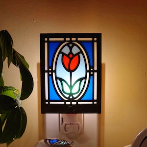 May include: A stained glass night light with a blue, red, and green tulip design. The night light is plugged into an outlet.