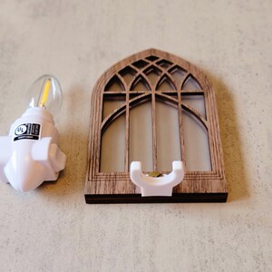 May include: A white night light with a UL label next to a wooden decorative window frame with a white holder. The window frame has a gothic arch design.