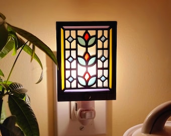 May include: A stained glass nightlight with a floral design in shades of blue, green, red, and yellow. The nightlight is plugged into an electrical outlet.