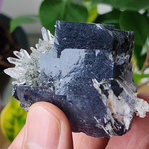 May include: A cluster of dark purple fluorite crystals with a layer of clear quartz crystals on top. The fluorite crystals have a layered, blocky appearance.