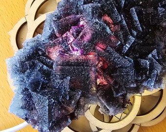 May include: A large, dark purple fluorite crystal cluster with iridescent hues. The crystal is resting on a wooden base with a decorative design.