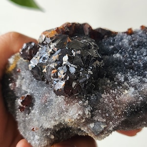 Könnte beinhalten: Ein Cluster aus schwarzen und braunen Kristallen auf einem Bett aus weißen und grauen Kristallen. Die Kristalle sind in einer natürlichen Formation angeordnet.