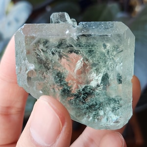 May include: A large, clear, green crystal with a unique, cloudy, and textured interior. The crystal is shaped like a cube with rounded edges.