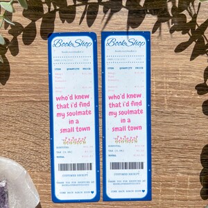 Op de afbeelding: Twee blauwe bladwijzers die op kassabonnen lijken. De bladwijzers tonen de tekst "Book Shop" bovenaan, gevolgd door artikeldetails en de zin "who'd knew that I'd find my soulmate in a small town."