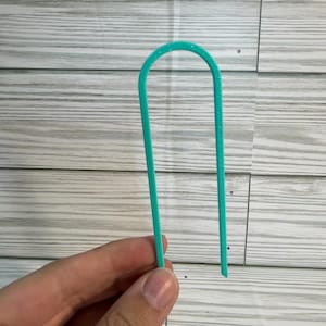 Puede incluir: Una horquilla para el pelo en forma de U de color turquesa brillante con un acabado de purpurina sutil. El accesorio para el cabello presenta una parte superior redondeada y lisa con dos puntas paralelas para sujetar el pelo.