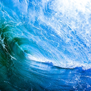 Puede incluir: Un primer plano de una gran ola azul del océano rompiendo. La ola está retroiluminada por el sol, creando un brillo blanco brillante. El agua es de un color azul profundo, con espuma blanca en la cresta de la ola.