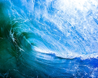 May include: A close-up of a large, blue ocean wave breaking. The wave is backlit by the sun, creating a bright, white glow. The water is a deep blue color, with white foam at the crest of the wave.