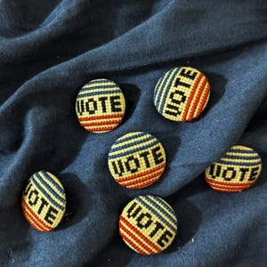 May include: Six red, white, and blue embroidered buttons with the word "VOTE" in black lettering.