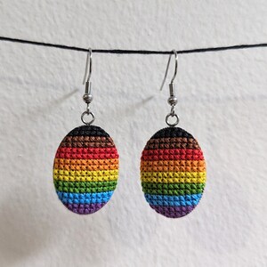 May include: A pair of rainbow pride earrings with a crocheted design. The earrings are oval shaped and feature a rainbow colour scheme with brown, red, orange, yellow, green, blue, and purple.