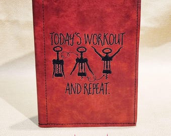 Op de afbeelding: Een rood lederen dagboek met zwarte stiksels en de tekst "TODAY'S WORKOUT AND REPEAT." De tekst is geborduurd met een ontwerp van drie flessenopeners. Het dagboek heeft een zwarte rug en de tekst "Star Shine Handmade" is in roze onder het dagboek gedrukt.
