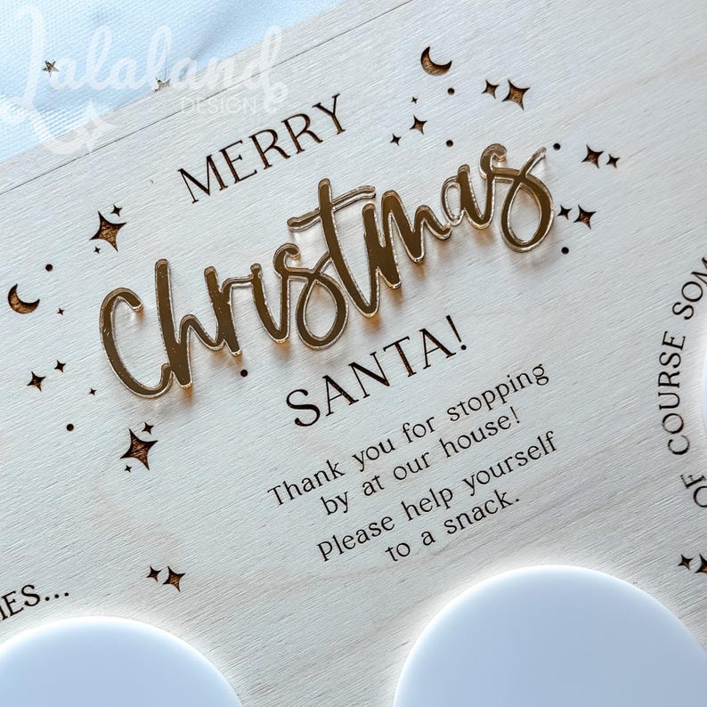 May include: A white wooden sign with the text "Merry Christmas Santa! Thank you for stopping by at our house! Please help yourself to a snack." The sign is decorated with gold glitter stars and moons.