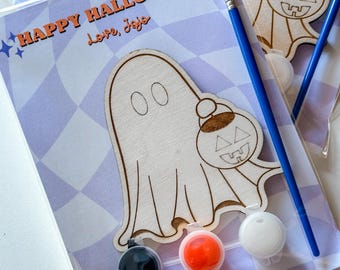 Puede incluir: Un fantasma de madera sosteniendo un recorte de calabaza con botes de pintura en negro, blanco y naranja. El texto "HAPPY HALLOWEEN love, Jojo" está en la tarjeta.
