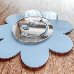 May include: A light blue flower-shaped mirror with a silver smiley face design.