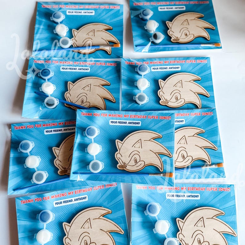 Puede incluir: Kits de Sonic el Erizo para pintar. Cada kit incluye una figura de Sonic de madera, botes de pintura y un pincel, todo empaquetado en una tarjeta azul con el texto "THANK YOU FOR MAKING MY BIRTHDAY SUPER SONIC!" y "YOUR FRIEND, ANTHONY."