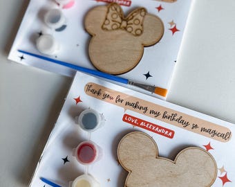 Puede incluir: Un kit de pintura de madera para pintar tú mismo con un diseño de cabeza de Mickey Mouse. El kit incluye cuatro pequeños botes de pintura en rojo, blanco, gris y amarillo, un pequeño pincel y una tarjeta de agradecimiento que dice "¡Gracias por hacer mi cumpleaños tan mágico! Con cariño, Alexandra".