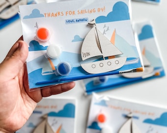 May include: A paint-your-own wooden sailboat craft kit with a blue paintbrush, three paint pots, and a card that says "Thanks for sailing by! Love, Andrew".