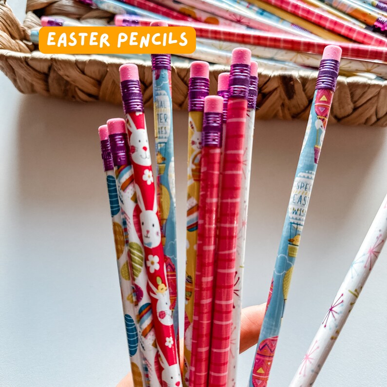 May include: A bunch of colorful pencils with Easter-themed designs, including bunnies, eggs, and flowers. The pencils have purple and pink erasers and are wrapped in white, blue, and pink paper.