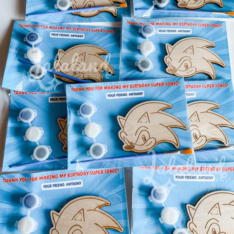 Puede incluir: Varios recuerdos de fiesta con el tema de Sonic el Erizo. Cada recuerdo incluye un recorte de madera de Sonic, botes de pintura y un pincel, todo empaquetado en una tarjeta azul con el texto "THANK YOU FOR MAKING MY BIRTHDAY SUPER SONIC!" y "YOUR FRIEND, ANTHONY."