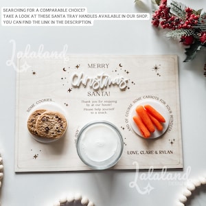 May include: A wooden tray with a white background and the words "Merry Christmas Santa!" in white letters. The tray has three white circles with snacks for Santa: cookies, milk, and carrots. The text on the tray reads "Some cookies... and of course some carrots for your reindeer! Love, Clare & Rylan."