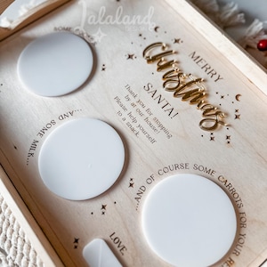 May include: Wooden tray with a gold glitter finish and the words "Merry Christmas" and "Santa!" in gold lettering. The tray has four white circles for placing items, with the text "...and some milk..." and "...and of course some carrots for your reindeer" written around the circles.