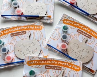 Puede incluir: Cuatro juegos de kits de manualidades de calabaza para pintar. Cada kit incluye un recorte de calabaza de madera, botes de pintura en verde, negro y rojo, un pincel y una tarjeta con el texto "Happy Halloween Pumpkin Pal! Love, Josephine".