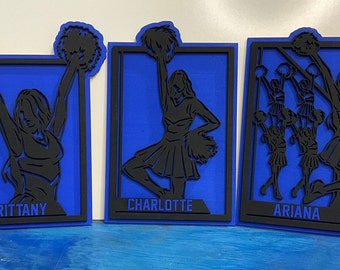 May include: Three blue and black cheerleading silhouette wall decor pieces with the names "Brittany", "Charlotte", and "Ariana" on each.
