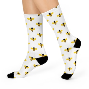 May include: A pair of white socks with a repeating pattern of yellow and black bees. The socks have black toe and heel.