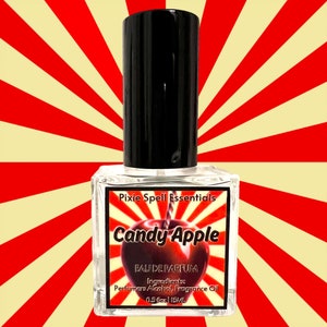 Puede incluir: Una botella de vidrio transparente con una tapa negra y una etiqueta roja y blanca que dice "Pixie Spell Essentials Candy Apple Eau de Parfum Ingredientes: Alcohol de perfume Aceite de fragancia 0.5 fl oz | 15mL"