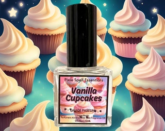 May include: A clear glass bottle of Pixie Spell Essentials Vanilla Cupcakes eau de parfum with a black cap. The label features a cupcake graphic and text including 0.5 fl oz | 15 mL. The bottle is centered against a background of illustrated cupcakes.