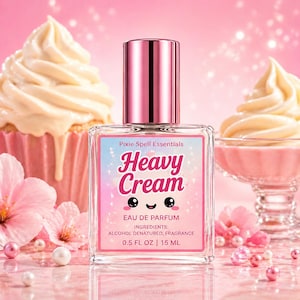 May include: A clear glass perfume bottle with a pink cap and label that reads "Heavy Cream" in a playful font. The label also includes the text "Pixie Spell Essentials" and "EAU DE PARFUM". The bottle contains 0.5 fl oz / 15 ml.