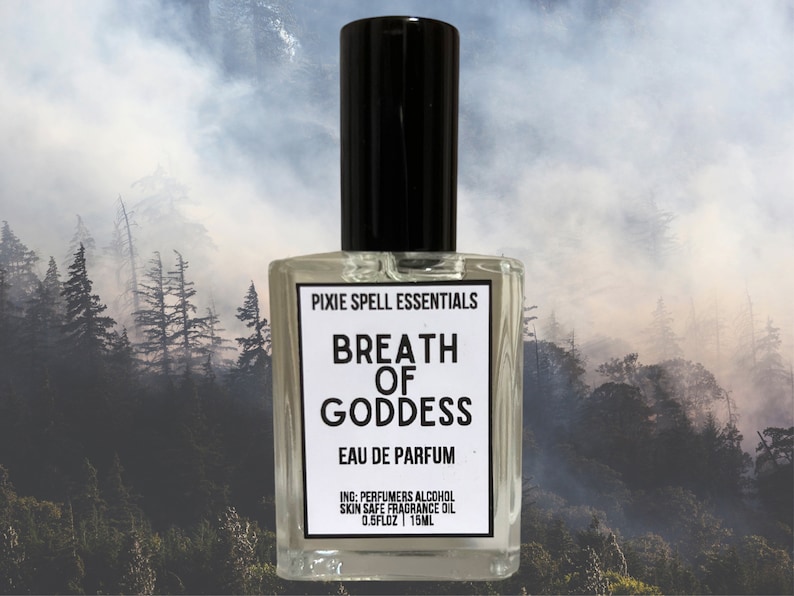 Op de afbeelding: Een heldere, rechthoekige parfumfles met een zwarte dop. Het etiket toont "PIXIE SPELL ESSENTIALS" en "BREATH OF GODDESS EAU DE PARFUM". Bevat 15 ml parfum. De achtergrond is een mistig bos.