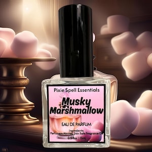May include: A clear glass bottle of Musky Marshmallow Eau de Parfum by Pixie Spell Essentials. The bottle is labelled with pink and black text and has a black cap. The bottle is sitting on a wooden surface with pink marshmallows in the background.