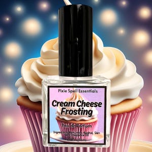 May include: A clear glass bottle with a black cap and a white label. The label says "Pixie Spell Essentials", "Cream Cheese Frosting", "Eau de Parfum", "Ingredients: Perfume Alcohol, Skin Safe Fragrance Oil", and "0.5 fl oz/15 ml". The bottle is in front of a cupcake with white frosting.