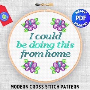 Peut inclure: Un motif de point de croix avec le texte "I could be doing this from home" et quatre fleurs violettes autour du texte. Le motif est affiché dans un cercle de broderie en bois.