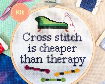 May include: A cross-stitch kit with a wooden hoop, scissors, and spools of thread. The cross-stitch design features a green chaise lounge and the text "Cross stitch is cheaper than therapy."