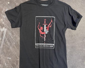 May include: Black t-shirt featuring a graphic print of a red figure falling through the air with a sword through them. The text "Yesterday's Fairytale, Tomorrow's Nightmare" and "昨日のおとぎ話 明日の悪夢" is printed below the graphic.