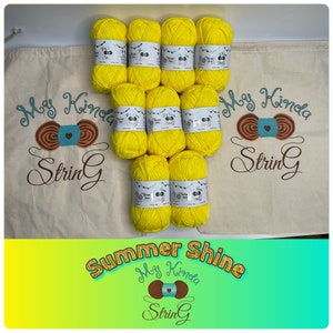 May include: Eight skeins of bright yellow yarn in a white drawstring bag with the text "My Kinda String" in brown lettering. The bag is sitting on a green and yellow background with the text "Summer Shine" in gold lettering and the text "My Kinda String" in brown lettering.