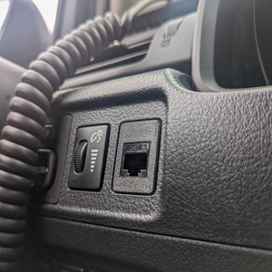 May include: Close-up of a black dashboard interior with a CAT 6 port and light controls. A coiled black cable is visible. The dashboard has a textured surface and several labeled buttons.